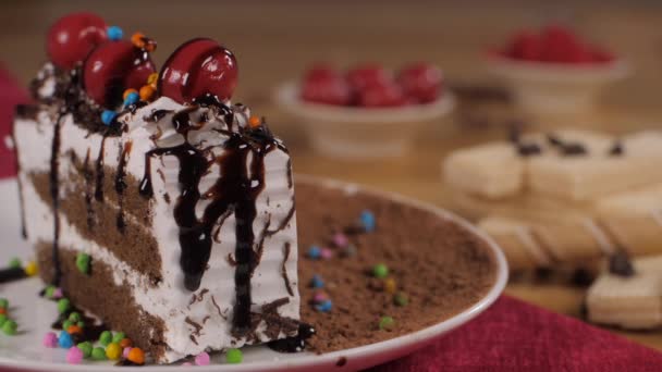 白いクリームケーキのスライスにガラスの液体チョコレートの霜を注ぐ カラフルな甘いスプリンクルとチェリーで飾られた自家製菓子ペストリースライスのクローズアップショット — ストック動画
