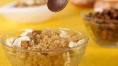 Şeffaf bir kase Sooji Ka Halwa 'da Hint tatlısında saklanmış tahta bir kaşık. Tatlı Hint irmik pudingi Kaju / kaju fındığı, Kishmish / kuru üzüm, sarı arka planda Badam / badem