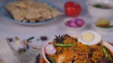 Hintli aşçının eli taze biryani ile birlikte bir tabak çıtır Papad tutuyor. Biryani 'nin yanında bir kase soğan turşusu, limon dilimleri, yeşil biber ve raita bulundurduğu yakın çekim tavuk.
