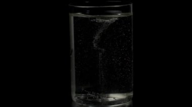 Şeffaf bir bardağın içindeki köpüklü temiz maden suyu. Siyah arka planda tutulan bardaktaki saf köpüklü suyun yakın plan çekimi.