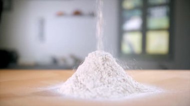 Evdeki mutfak tezgahında oluşan buğday ununun yakın plan çekimi. Taze buğday zemininin ahşap bir platformda bulanık mutfak arka planına düşmesi - yemek ve pişirme konsepti