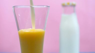 Kremalı süt, temiz bir bardak mango karışımının içine dökülür. Sağlıklı bir içecek, Hindistan Yazı içeceği. Bir şişe taze sütün yakın plan çekimi bir bardak taze tropikal Aam suyunun yanında tutulur - yaz meyvesi