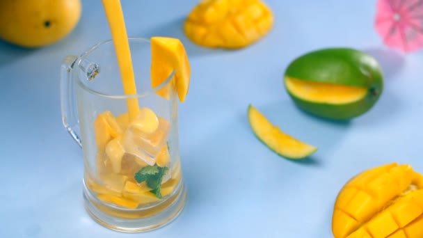 ミントとフルーツキューブと新鮮な夏の冷たいマンゴーカクテル おいしい飲み物 青いマットに保管された小さな傘でジューシーなマンゴーのクローズアップショット 夏のドリンクインド — ストック動画