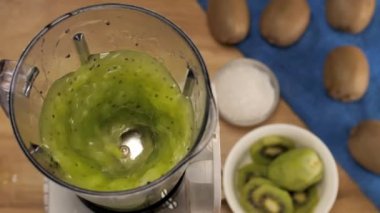 Olgunlaşmış yeşil kivili smoothie blender içinde canlandırıcı bir içecek hazırlıyor. Sağlıklı yaşam için ahşap bir masada karıştırılmış lezzetli kivi suyunun yakından çekimi - taze meyve diyeti konsepti