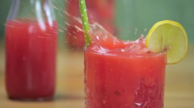 Karpuz suyuyla dolu şeffaf bir bardağa düşen büyük bir buz küpü - Hindistan yazı meyvesi. Yakın çekim, limon dilimi ve pipetle tropikal mevsimlik meyve kokteyli. Yeni sıkılmış egzotik içecek.