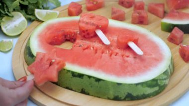 Hanımefendinin eli ahşap bir masaya taze karpuz dondurması tutuyor / yerleştiriyor. Yakın plan Tarbooj dilimleri, narenciye limonu ve nane yaprakları bir arada tutulur. Tropikal yaz meyvesi Hindistan.