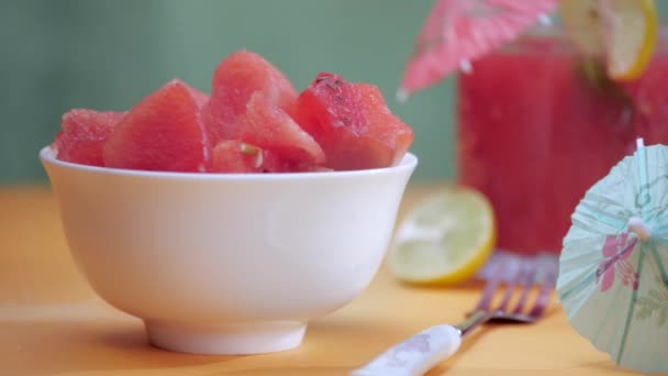 切块多汁的西瓜掉在瓷碗里 热带夏季水果 用柠檬片和红色雨伞装饰的新鲜塔布酒放在木制桌子上的特写镜头 — 图库视频影像
