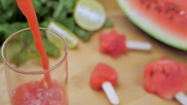 新鲜而成熟的西瓜汁 冰沙倒入一杯清澈的玻璃杯中 印度夏季水果 薄荷树 柑橘类柠檬和薄荷叶切碎后放在一张木制桌子上的特写镜头 — 图库视频影像