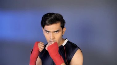 Spor giyimli genç kickboksör elleri boks antrenmanına sarılmış boks kasetiyle. Orta boy, kaslı Hintli sporcunun kapalı alanda, formda ve aktif bir yaşam tarzına karşı kendine güvenle yumruk atma görüntüsü.