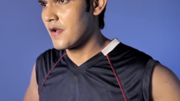 一个疲惫的印度运动员的Sideview 满脸汗珠 呼吸急促 一个黑发的年轻运动员站在彩色背景的黑色T恤上的倾斜画面 — 图库视频影像