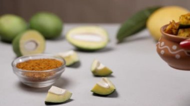 Hint yazlarında mango turşusu yapmak için kadının eli baharatlı çiğ mango tutuyor. Yakın çekim çiğ mango, turşu masala ve ahşap bir masada saklanmış olgun bir mango.