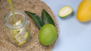 Hindistan 'da yaz içeceği olan Aam Panna' yı dilimlenmiş limonla taze mango suyu ve şurubu şişeye döküyorum. Olgun ve çiğ bir mangoyu yakın plan çekimde ahşap bir masanın üzerinde sakladım. Kokteyl malzemeleri.
