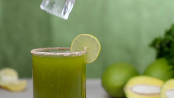 さわやかな飲み物の澄んだガラスの中に2つの氷のキューブ アダム パンナ 背景がぼやけている生の緑のマンゴーと新鮮なミントの葉のクローズアップ インドの夏の飲み物 — ストック動画