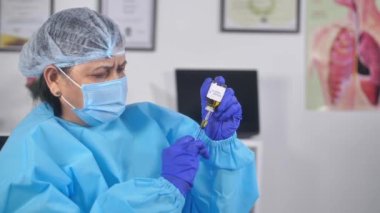 Cerrahi maskeli bir tıp çalışanı şırıngayı COVID aşısıyla dolduruyor. Kıdemli bir doktor eldiven takıyor Coronavirus aşılama kampanyasından aşı alıyor.