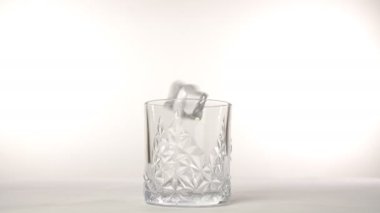 Boş bir viski bardağının içine dört büyük buz küpü beyaz arka plana düştü. İçki için hazırlanan güzel bir bardak alkolün yakın plan çekimi. Viskiyle rahatlama zamanı.