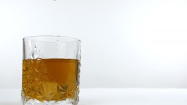 Büyük buz küpleri şeffaf bir bardak altın viskinin içine düşüyor. Viski ve sert içeceğin yakın görüntüsü beyaz arka planda buz küpleriyle dolu bir bardakta.