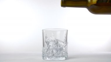 Kahverengi bir şişeden kristal berrak bir bardağa altın viski döküldü. Viski ve sert içecek, beyaz arka planda buz küpleri olan şeffaf bir bardağa dökülüyor.