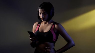 Spor yaparken cep telefonu kullanan bir kadın. Sağlıklı bir yaşam tarzı. Kısa saçlı Hintli sporcu eğitim sırasında spor programını kontrol etmek için akıllı telefon kullanıyor.