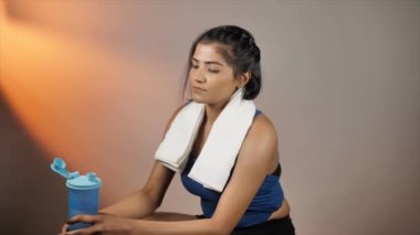 Spor salonundan sonra protein içeceği içen sağlıklı bir kadın. Havluyla boynuna dolanmış şık, ince bir kadın. Spor salonundan sonra oturuyor. Sağlık ve zindelik.