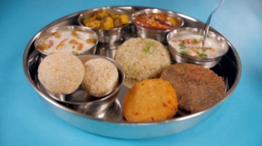 Kuzey Hindistan 'daki bir Vrat Thali' den Raita alırken yakından çekilmiş bir kaşık. Geleneksel yemek tabağında Kuttu Puri, Sabudana Khichdi, Cholai Laddu, Kheer, Sabzi, Tikki ve Raita mavi arka planda.