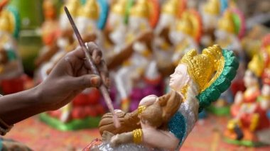 Kadın sanatçı Hindu Tanrıça Saraswati 'nin kilden heykeline simli bir renk koyuyor. Arkaplanda Saraswati puja için hazırlanmış diğer heykellerle birlikte Hindu Tanrıça heykeli çizen sanatçı