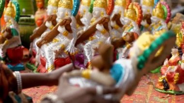 Hintli kadın zanaatkar, kil bir heykelin ellerine simli boya sürüyor. Sanatçı, Hindu tanrıça idolü / murti 'nin boyamasını bitiriyor. Arka planda Saraswati puja' nın diğer heykelleri de hazır.