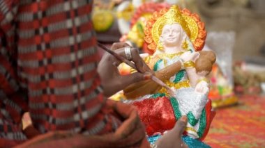 Hint zanaatkar Ma Saraswati 'nin kil heykeline son rötuşları yapıyor. Saraswati puja için güzel bir Hindu tanrıçasının ellerini boyayan bir sanatçının yakın çekimi.