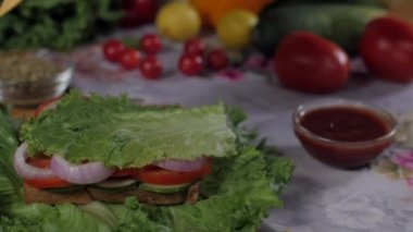 Açık vejetaryen sandviçin üzerine peynir dilimi dökülüyor. Bir kase aromalı kekik ve bulanık arka planda sağlıklı yeşil marul yapraklarının yakın plan çekimi.