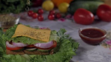 Leziz bir sandviçi hazırlamak için kullanılan peynirin üzerine düşen lezzetli kekik. Domatesler, sulu limonlar ve yeşil kapsicum gibi renkli sebzeleri yakından çek.