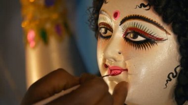 Hintli bir sanatçının elleri Tanrıça Durga 'nın kil heykelinin dudaklarını boyuyor. Durga Puja festivali için Hindu idolü Ma Durga 'nın dudaklarını boyayan bir zanaatkarın yakın çekimi.
