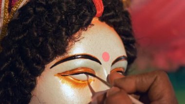 Hintli bir sanatçının, Tanrıça Durga 'nın kil heykelinin gözlerini çizdiği yakın çekim. Durga Puja festivali için bir boya fırçasıyla Ma Durga 'nın idolünün gözlerini çizen bir zanaatkarın elleri.