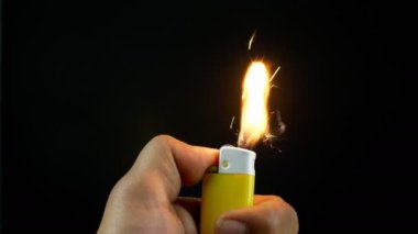 Siyah arka planda sigara için sarı bir çakmak. Portatif bir çakmağı tutan bir elin yakın çekim görüntüsü - sigara yakmak için bir cihaz