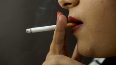 Yakın çekim, siyah arka planda sigara içen Hintli kız. Bağımlı genç bir kadının zehirli bir sigara tüttürmesi ve duman üflemesi sağlıksız bir yaşam tarzı.