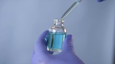 A scientist in a laboratory with a dispenser in his hands doing an analysis. Closeup shot of a male doctor wearing blue gloves putting /mixing medicine in a glass bottle