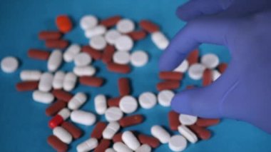 A medical health worker's hand taking a white-colored pill from the table . Closeup shot of multicolored tablets kept together against a blue background - treatment and recommendation
