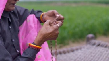 Hindu kültüründe tespih kullanırken dua eden yaşlı bir kadını yakından çek. Geleneksel yaşlı bir kadın, köyün yakınındaki bir tarım arazisinde dua ederken ahşap boncuklar kullanıyor.