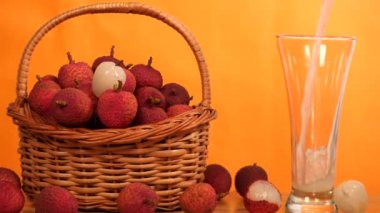 Geleneksel ve sağlıklı Lychee suyu uzun bir bardağın içinden dökülüyor. Soyulmamış bir yığın Litch 'in yakın planda çekilmiş bir fotoğrafı. Bir tanesi ahşap sepetin içinde, renkli bir arka planda saklanıyor.