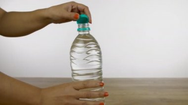 Kadın eli, tatlı suyla dolu plastik bir şişenin kapağını kapatır. Kırpılmış Hintli kadın, beyaz arka plana karşı ahşap bir platforma yerleştirilmiş maden suyu şişesini kapatıyor.