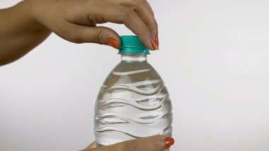 Hintli bir kadının bir şişe maden suyu açarken yavaş çekim görüntüsü. Kadın elinin yakın plan çekimi beyaz arka planda plastik bir su şişesinin kapağını açıyor - sağlık ve diyet konsepti