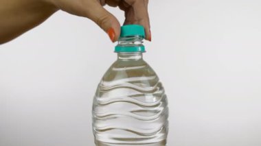Hintli bir kadının maden suyu şişesini kapatırken yavaş çekim. Kadın elinin yakın plan çekimi beyaz arka plandaki plastik bir su şişesinin kapağını kapatıyor - sağlık ve diyet konsepti