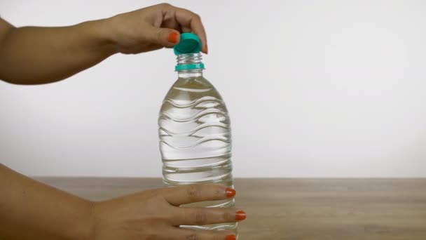 女性の手の閉鎖は 淡水で満たされたペットボトルのキャップを閉じます 白い背景に木製のプラットフォーム上に置かれたミネラルウォーターのボトルを閉じるインドの女性をトリミング — ストック動画