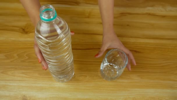 ボトルからグラスに淡水を注ぐ女性の手の高角度ショット 木製のプラットフォーム上のプラスチックボトルからそれを追加した後 水のガラスを飲むクロップインドの女性の閉鎖 — ストック動画