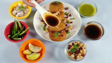 Hintli aşçının eli Aloo Tikki 'ye Meethi Chutney / Saunth katmanları koyuyor. Dhania Chutney, dilimlenmiş yeşil biber, sulu limon gibi malzemeleri ahşap bir masada bir arada tutardı.