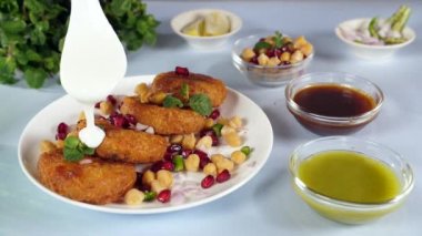 Ev yapımı çıtır Aloo Tikki 'nin üzerine kremalı yoğurt katmanları koymak - lezzetli yemekler - Hindistan' dan sokak yemekleri. Bir demet nane yaprağı, dilimlenmiş limon, yeşil biber ve soğanların yakın plan çekimi. Yemek malzemeleri.