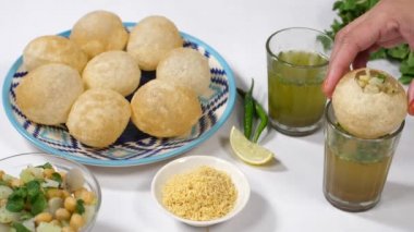  Golgappas 'ı Aloo ve nohutlarla doldurup Hindistan' dan gelen bir bardağın üstüne koymak. Yakın plan Pani Puri, yeşil biber, limon, beyaz arka planda bir kase Bhujia.