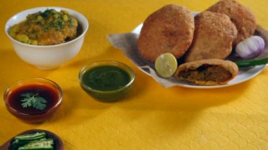 Elleri baharatlı yeşil biber ve bir tabak lezzetli Kachoris ve çiğ soğan tutuyor. Dal Kachori 'nin yakın plan çekimi bir kase Aloo Ki Sabzi' ye batırılmış ve Chutney ahşap bir masada bir arada tutuluyor.