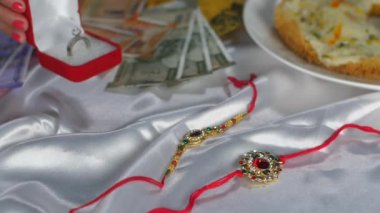 Genç eller, kardeşi tarafından hediye edilen güzel bir yüzüğü Hindu Festivali 'nde Rakhi' ye takıyor. Raksha Bandhan festivali için yakın plan banknotlar, tasarımcı Rakhis ve lezzetli yemekler.