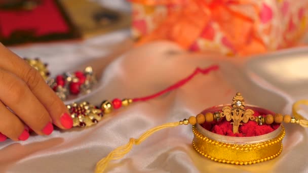 女性的手抓住一个美丽的若开邦 因为她绑在她哥哥的手腕印度教节上 在Raksha Bandhan节 一个包装精美的礼品盒和五彩缤纷的信封在一起 — 图库视频影像