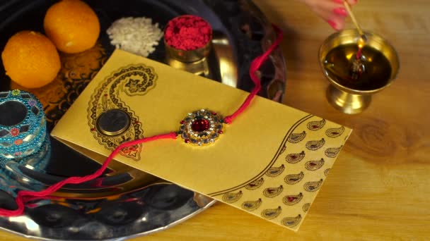 女性の手が自宅でラクシャ バンダン フェスティバルでオイルランプ ディヤを点灯 ヒンズー教の祭り お菓子 Lifaafaと花が木のテーブルの上に保管された法会 アート タイの閉鎖ショット — ストック動画
