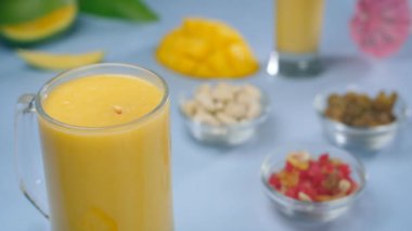 Tutti Frutti / tatlı şekerler şeffaf bir bardak ferahlatıcı içeceğe dökülüyor - Hindistan Yazı İçeceği. Kuru meyve yakın çekim, bir bardak sağlıklı meyve milkshake ile mango dilimleri bir masada birlikte